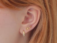 Video of woman's ear featuring 14K Gold Tiny Bow Single Stud, heart stud, and drop hoop earring 