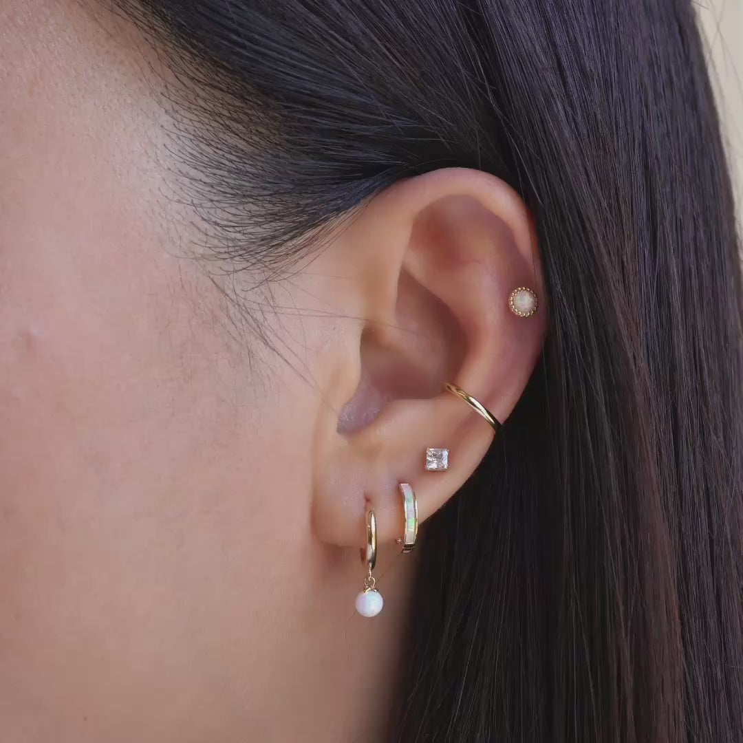 Model wearing 14k gold opal earrings, conch cartilage hoop and flat back studs.
