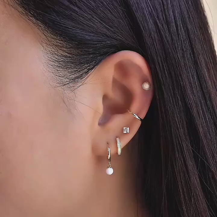 Close up shot of model wearing 14K Gold Opal Huggie Earrings, Princess cut studs, cartilage hoop and beaded opal flat back earring from AMYO.