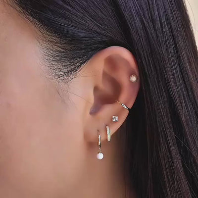 Close up shot of model wearing 14K Gold Opal Huggie Earrings, Princess cut studs, cartilage hoop and beaded opal flat back earring from AMYO.