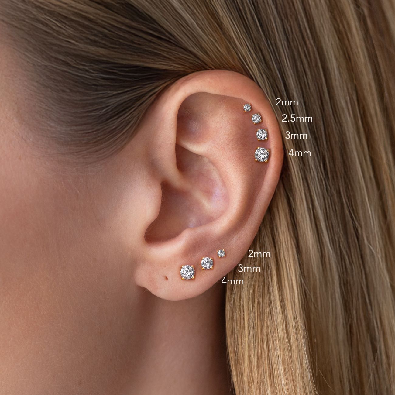 Close-up of an ear with classic round pavé stud earrings of different sizes, labeled.