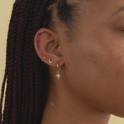 Woman wearing gold starburst huggie earring, gold crescent moon pave stud, gold flare star single stud, and gold tiny star single stud 