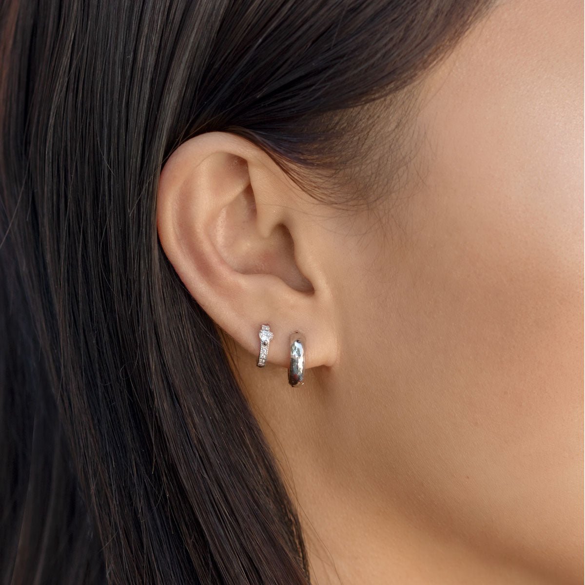 Close up of woman's ear featuring Sterling Silver Tiny Heart Huggies paired with silver huggie earring 