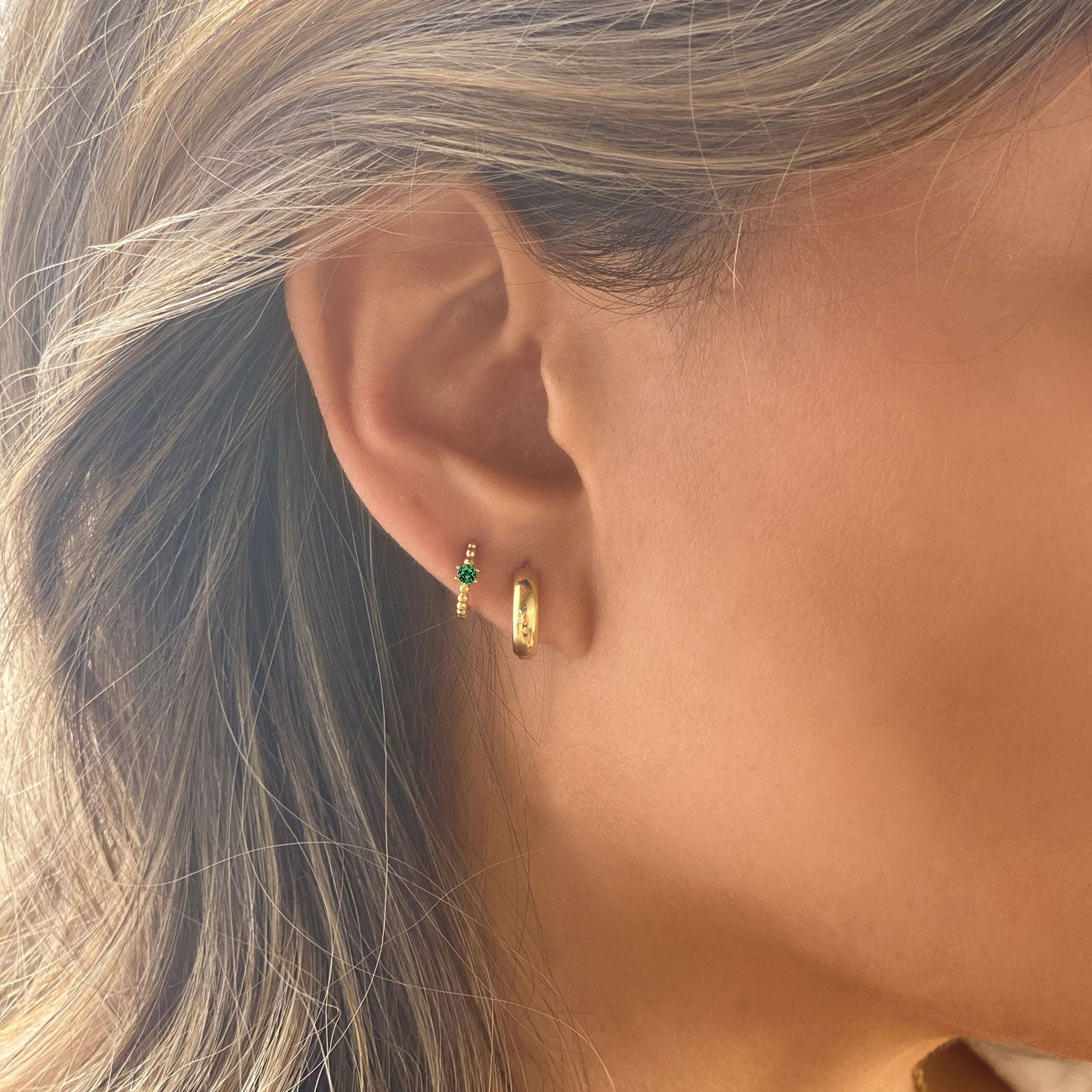 Close-up of woman's ear featuring Gold Vermeil Gemstone Bead Huggies Emerald CZ Crystal and Gold Chunky Hoop. 