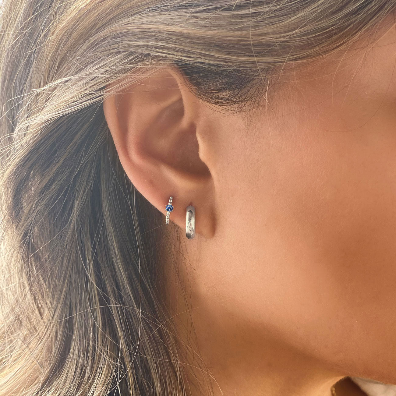Close-up of woman's ear featuring Sterling Silver Gemstone Bead Huggies Blue Zircon CZ Crystal and Silver Chunky Hoop. 