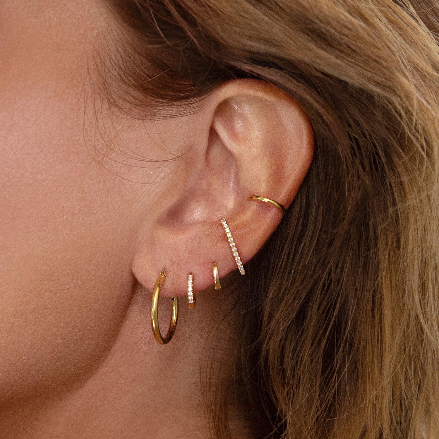 Gold ear stack made of hoops, huggie earrings, suspender earrings and ear cuff