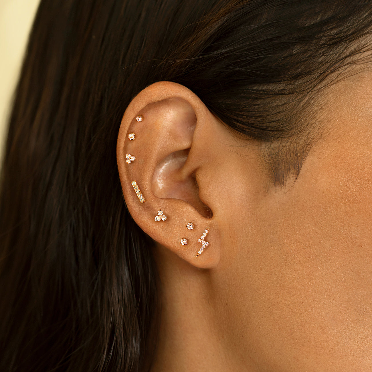 Gold clover and lightning bolt studs shown styled in a cartilage stack on a model's ear