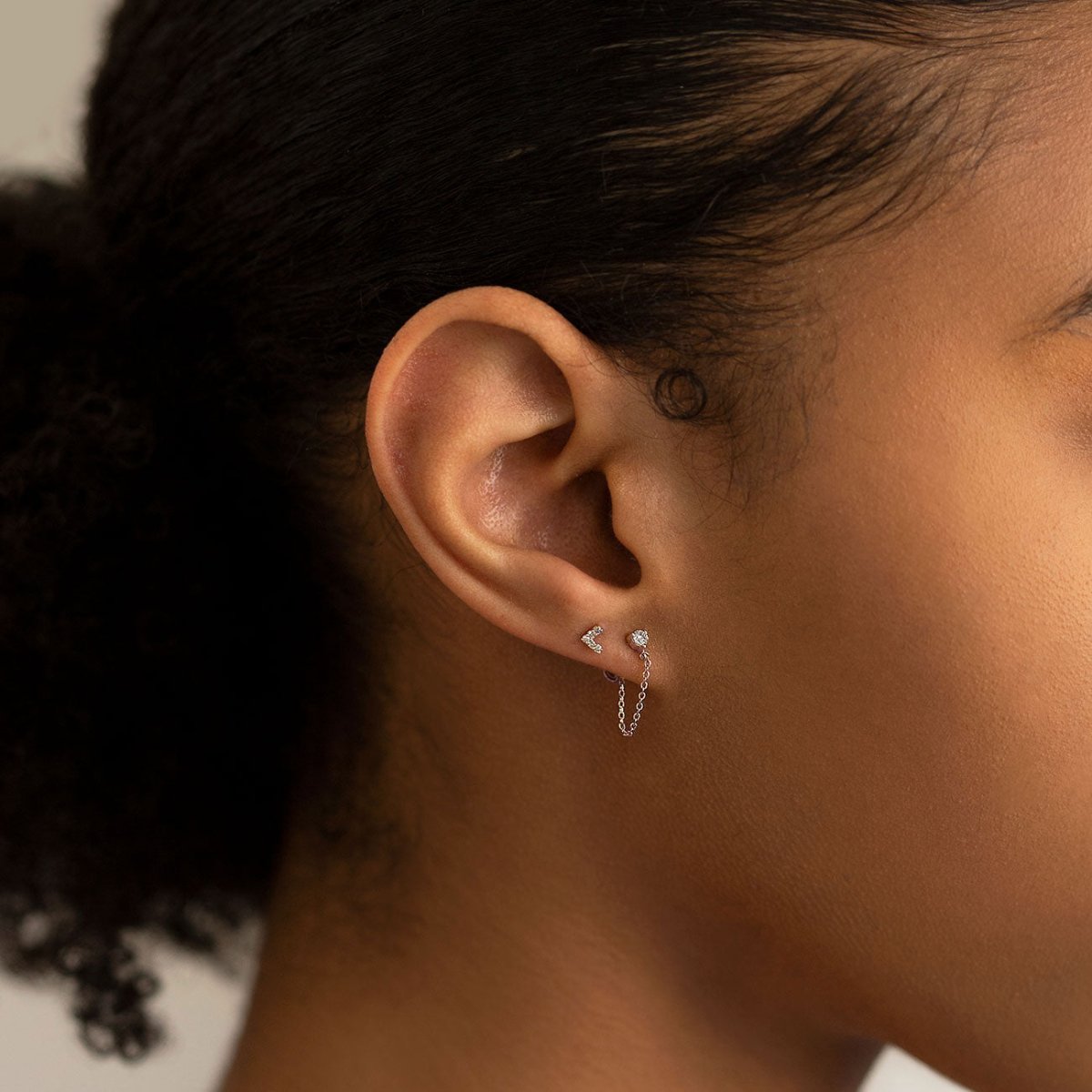 Tiny silver chevron and round studs with clear stones shown stacked on a model's lobe.