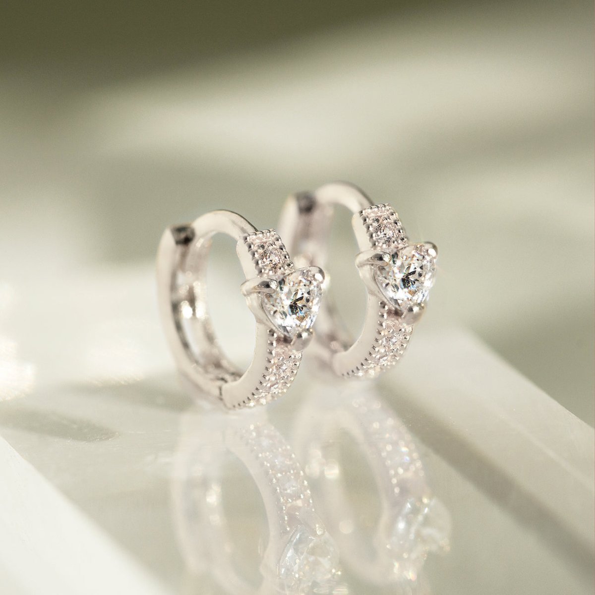 Close up of earring featuring Sterling Silver Tiny Heart Huggies