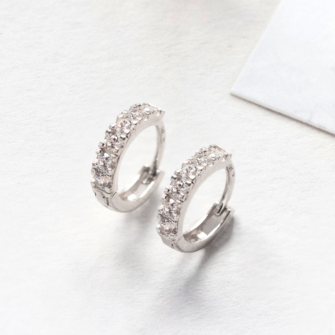 Close-up of 14K white gold moissanite crysta pave huggie earrings. 