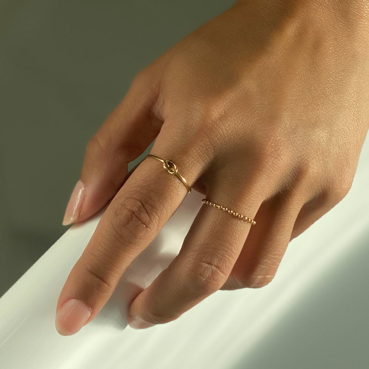 Hand wearing dainty gold knot ring and bead chain ring