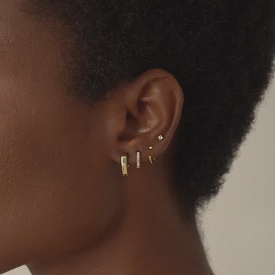 Close-up of woman's ear featuring 14K Solid Gold Octagon Huggie Earrings, Pave Huggie Earring, Sphere Huggie Earring, and Tiny Crystal Stud Set 